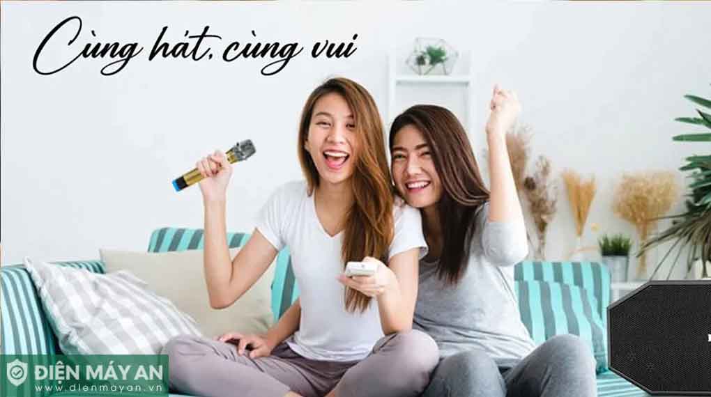 Hai cô gái hát karaoke tại nhà với micro không dây và loa karaoke trên ghế sofa